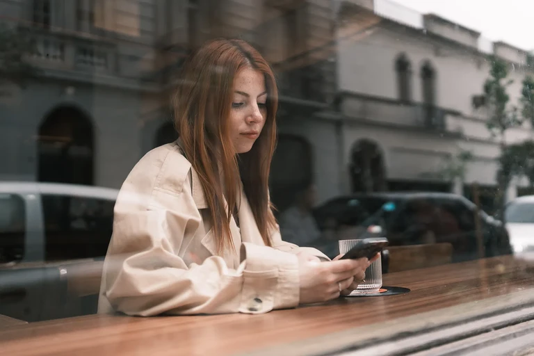 Mujer sentada en mesa de café al aire libre usando un movil