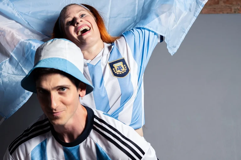 Hinchas de fútbol argentino posando con bandera y gorro celeste y blanco