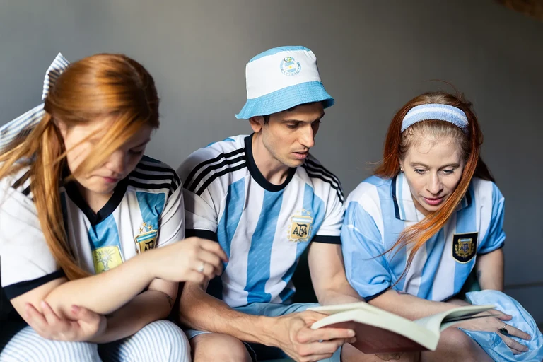 Tres hinchas sentados compartiendo un momento mientras leen un libro