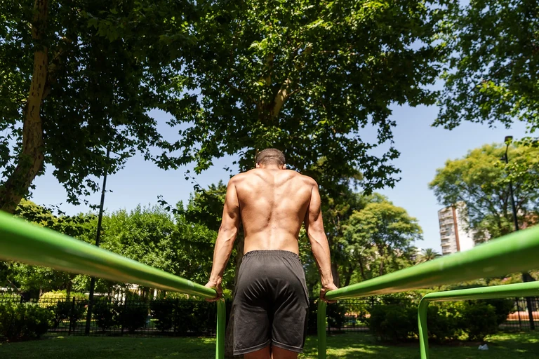 Hombre haciendo dominadas de espalda en barras de parque al aire libre