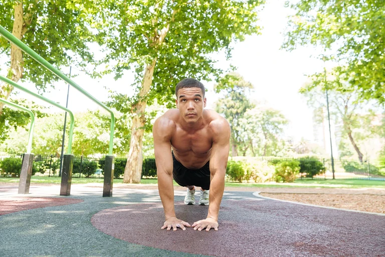 Hombre realizando flexiones de brazos en el suelo de un parque