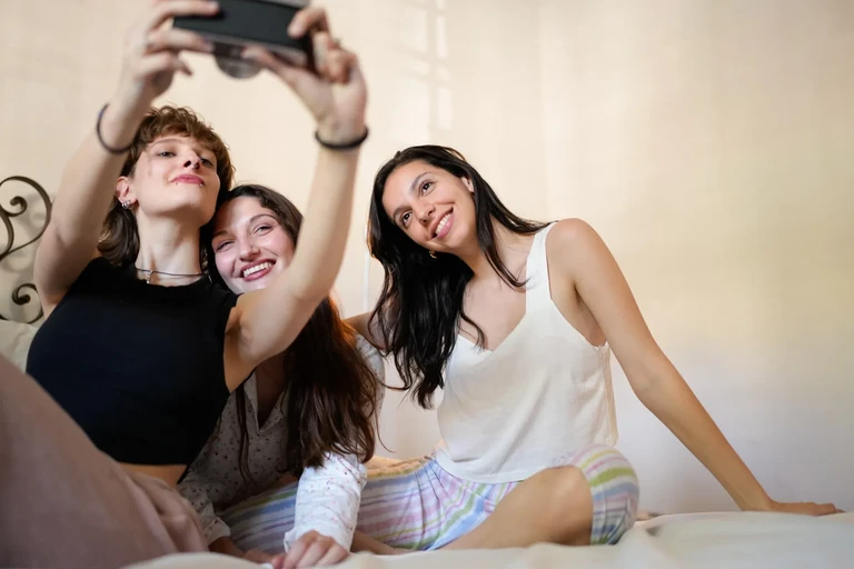 Grupo de amigas riendo y tomándose una selfie en la cama