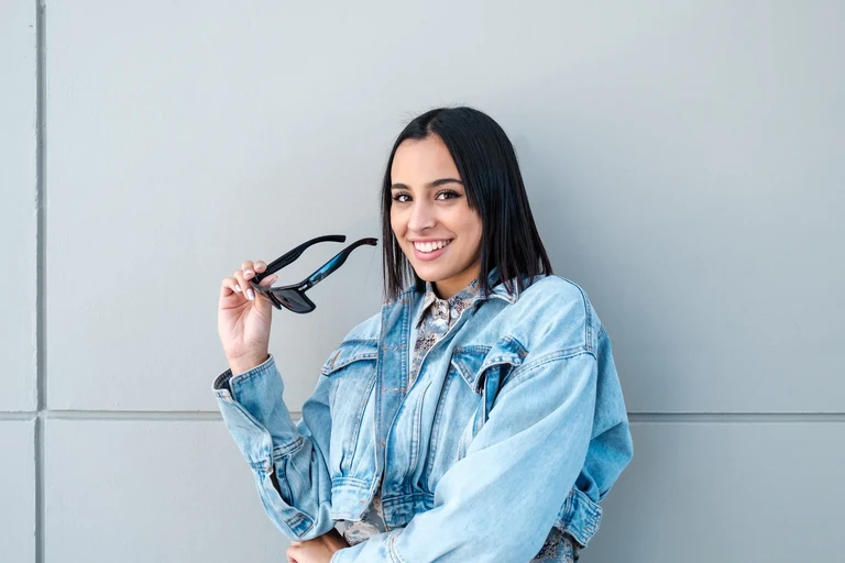 Mujer sonriente posando con anteojos de sol y chaqueta de jeans